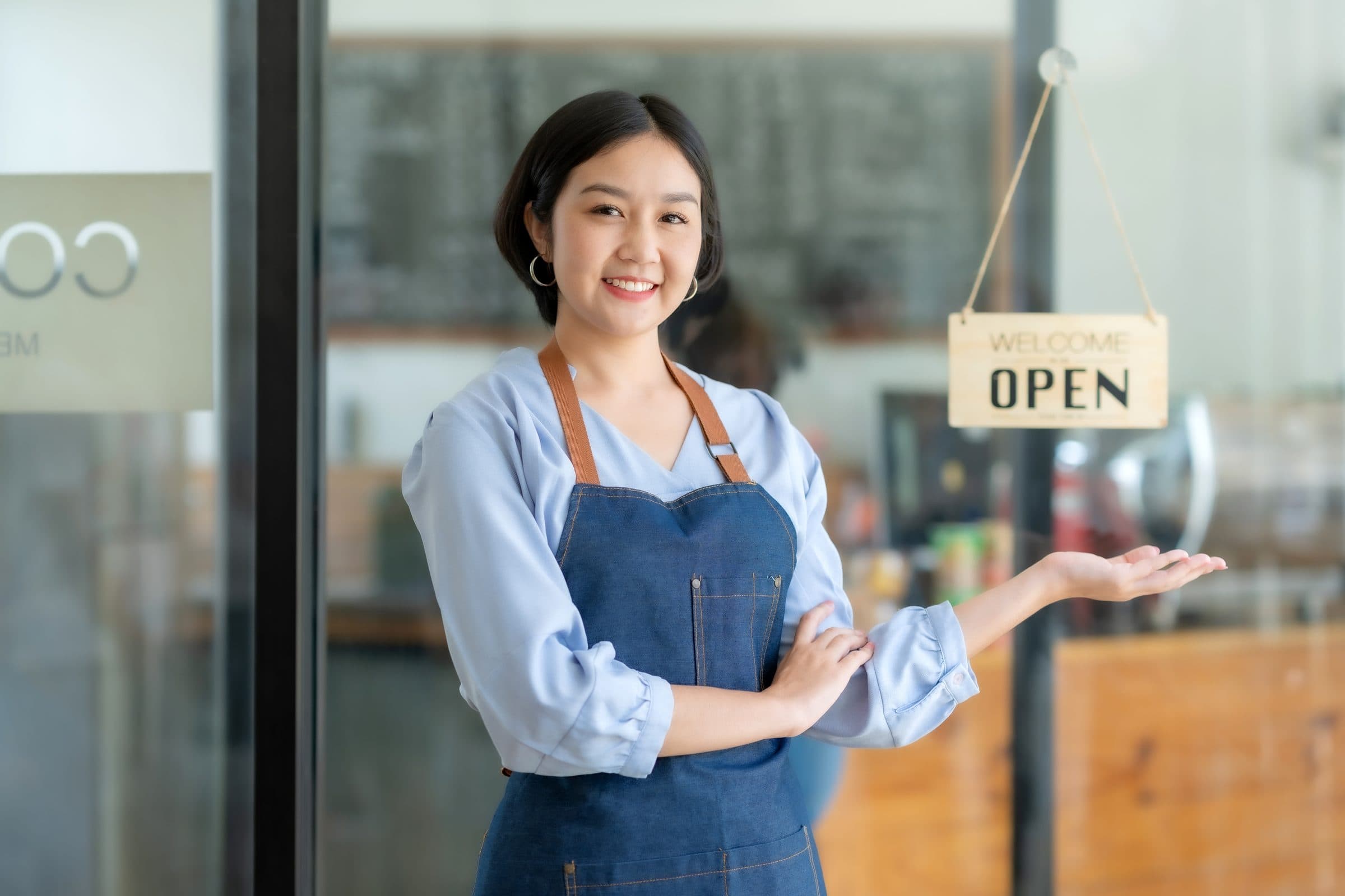 A café owner in an apron smiling beside the door's Open sign